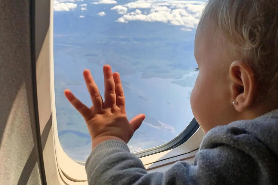 Bebê olhando pela janela do avião após mãe escolher carrinho de bebê que cabe no avião